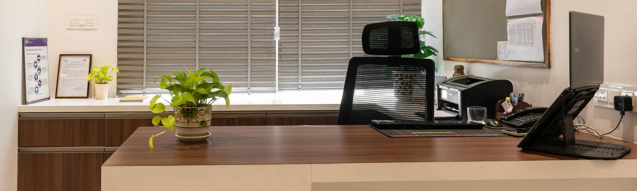 A desk is pictured, with a chair, plant, and computer.