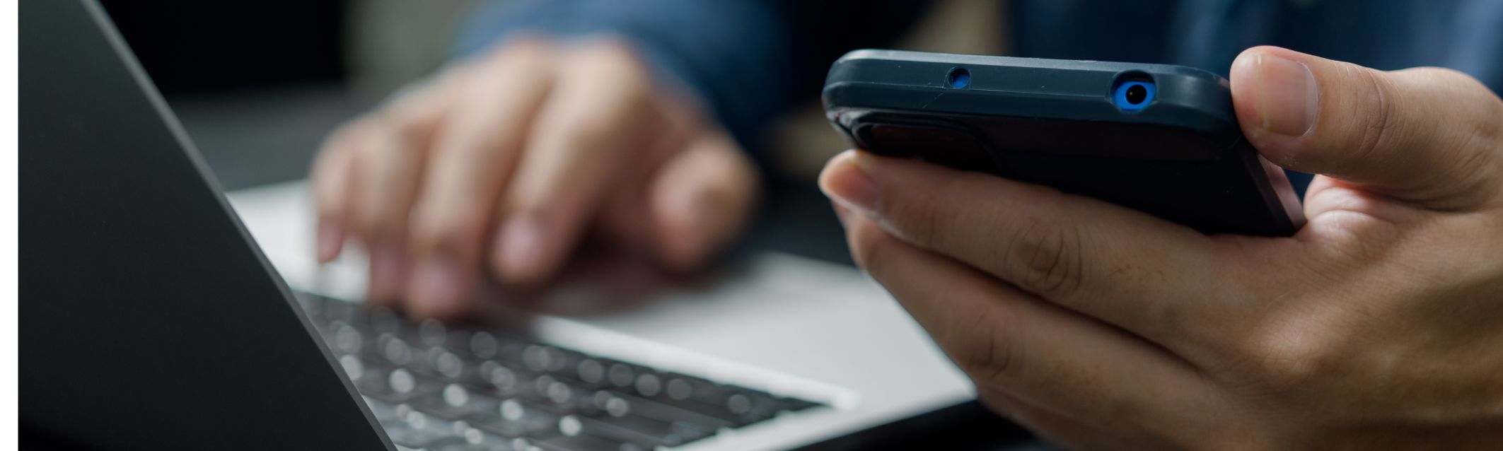 Someone types at a computer and holds a mobile phone